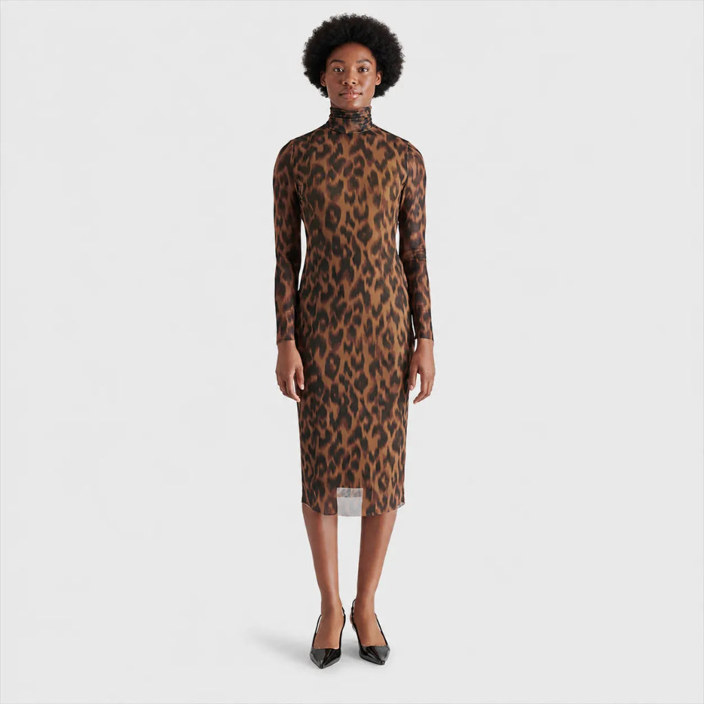 A woman modeling a long-sleeve mock-neck midi dress with a brown and black leopard print pattern, paired with black pointed-toe heels, against a light gray studio background.