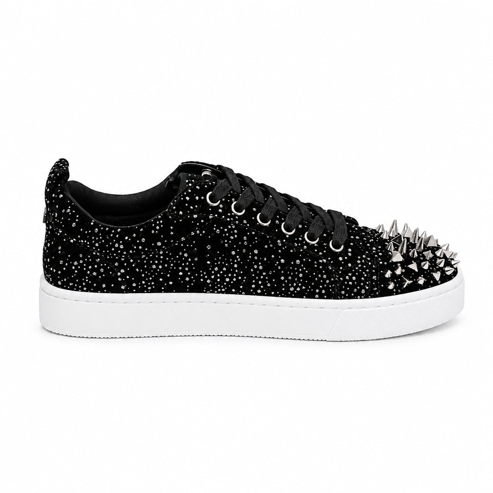 A black low-top sneaker covered in silver rhinestones and topped with prominent silver spiked studs on the toe, shown against a plain white background.