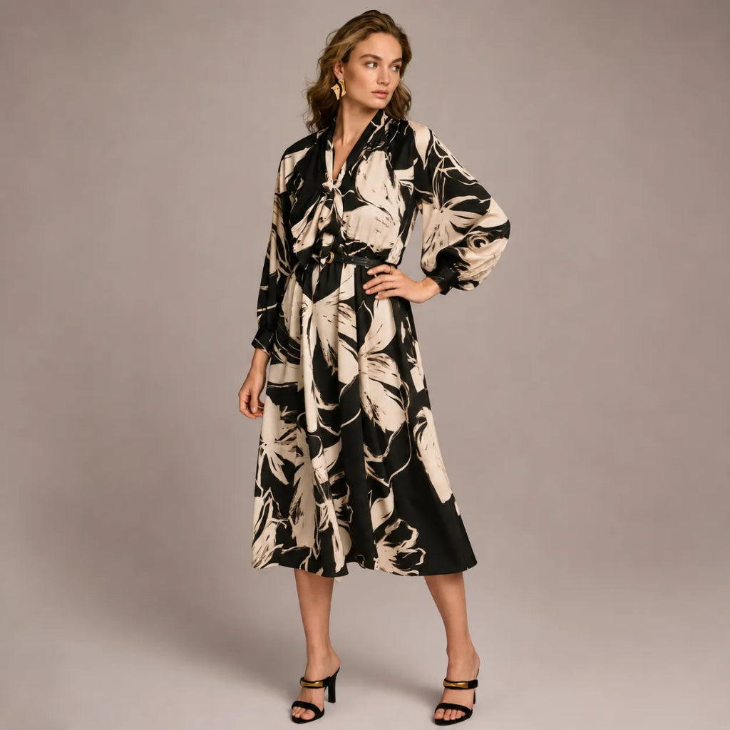 A woman models a long-sleeve midi wrap dress with a black and beige abstract floral pattern, standing against a solid gray studio background.