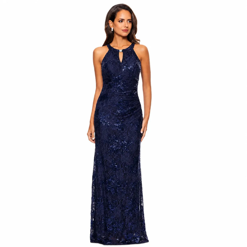 A woman modeling a sleeveless, floor-length navy blue gown covered in shimmering sequins and floral lace, set against a plain white background.