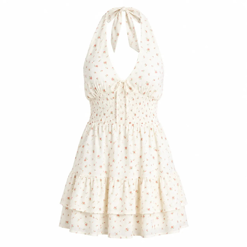 An off-white halter mini dress with a delicate pink floral print, featuring a smocked bodice, tie-front neckline, and tiered skirt.