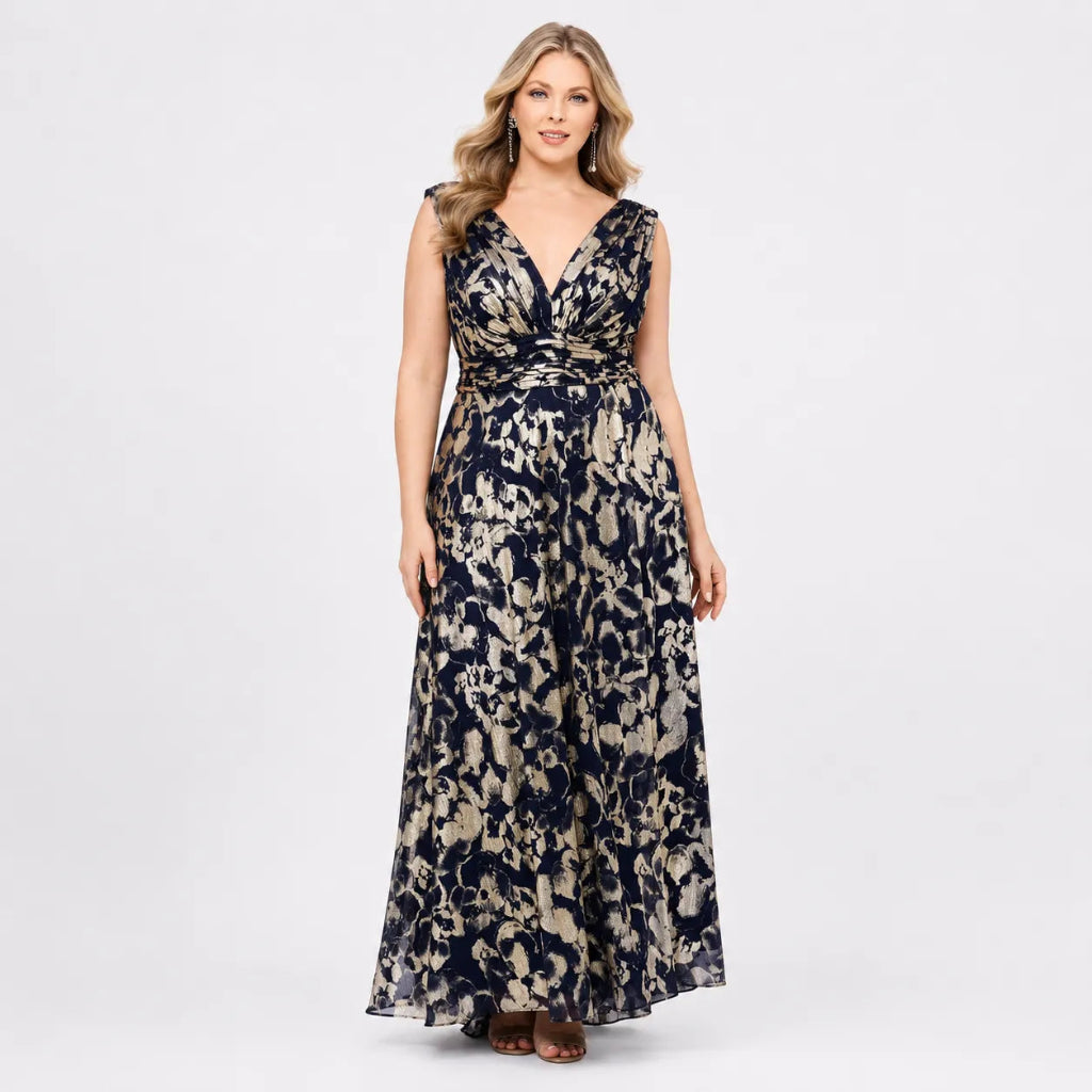 A woman modeling a sleeveless, floor-length V-neck maxi dress with a navy blue and beige abstract floral pattern, standing against a light gray studio background.