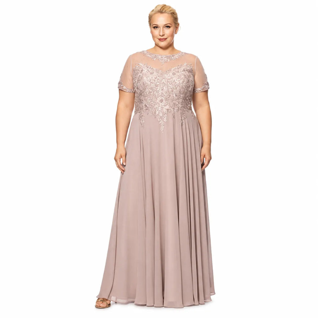 A plus-size blonde model wearing a floor-length dusty pink formal gown with a sheer embroidered bodice and short sleeves, photographed against a plain white background.