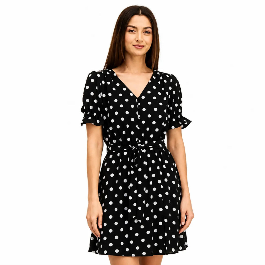 A woman modeling a black wrap-style mini dress with white polka dots, short flutter sleeves, and a tie waist, photographed against a plain white background.