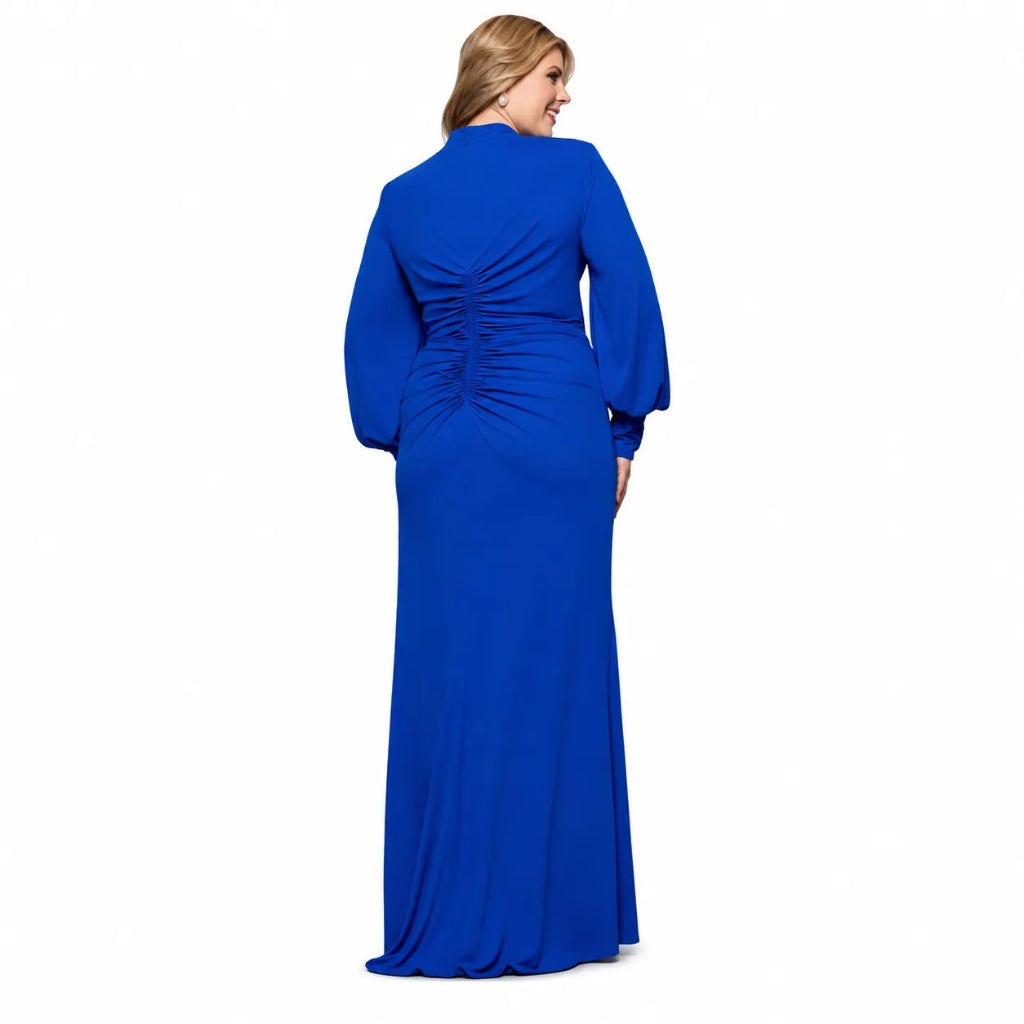 A woman modeling a floor-length royal blue gown from the back, featuring long sleeves, a high neckline, and a gathered ruched back detail, set against a plain white background.