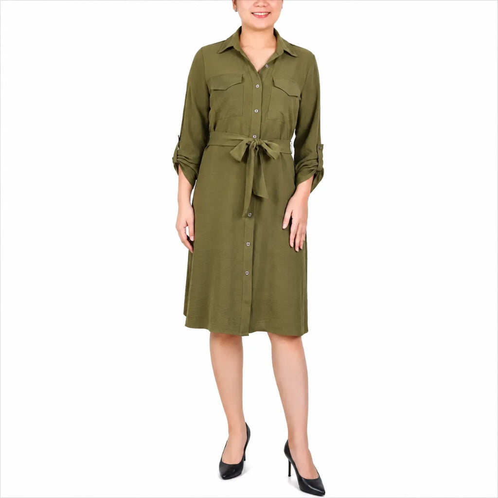 A woman modeling an olive green military-style shirt dress with three-quarter sleeves, button-down front, chest flap pockets, and a matching waist tie, paired with black high heels on a white background.