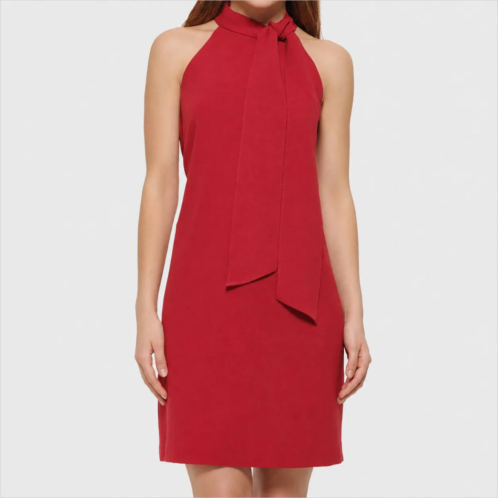 A woman wearing a sleeveless red halter dress with a tie-neck detail, shown against a light gray studio background.