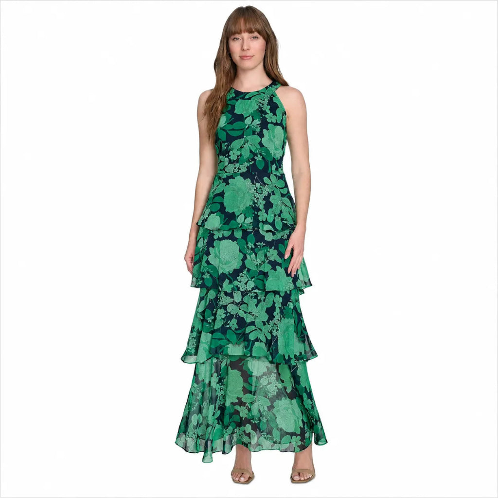 A woman modeling a sleeveless, high-neck, tiered maxi dress with a green and black floral pattern, set against a plain white background.