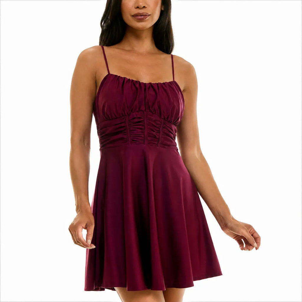 A woman wearing a sleeveless, skater-style mini dress in deep burgundy with a gathered bodice and thin shoulder straps, shown against a plain white background.