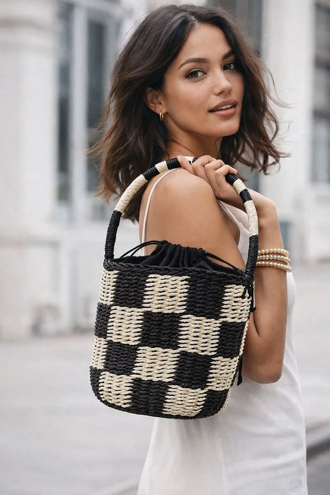 Woman holding a black and white woven handbag in an urban setting