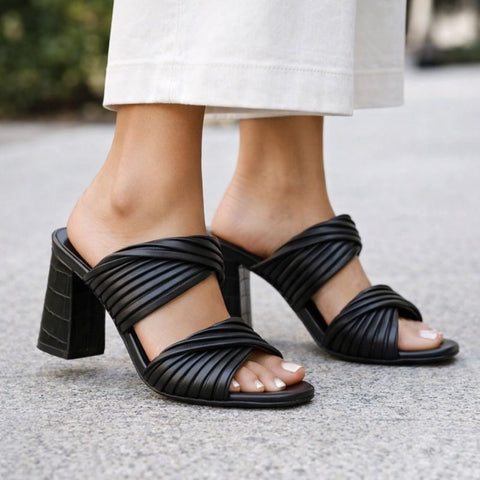 Black strappy high-heeled sandals worn by a person on a blurred background
