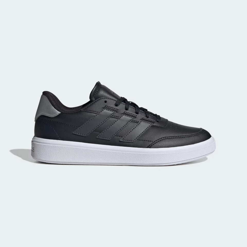 A black Adidas low-top sneaker with a white midsole and a metallic gray heel accent, shown in a side profile on a light gray background.