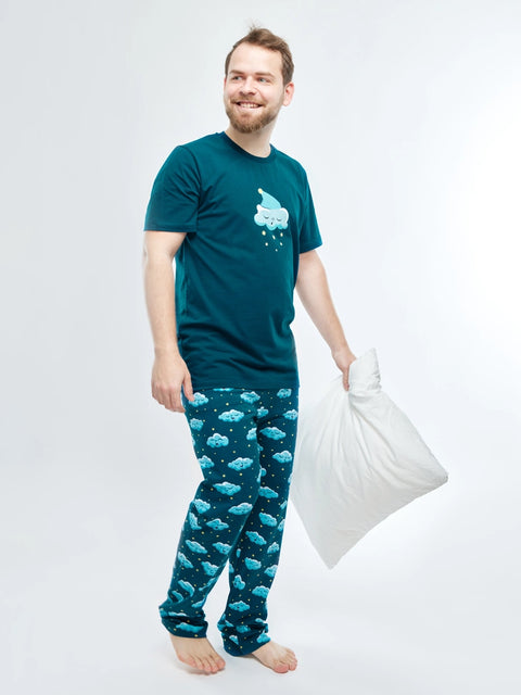 Man wearing a teal t-shirt and matching pants with cloud pattern, holding a pillow on a white background