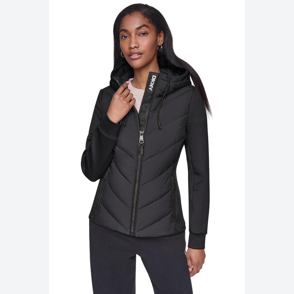 A woman modeling a black hooded puffer jacket with a full front zipper and a visible 'DRY' brand label on the collar, set against a plain white studio background.