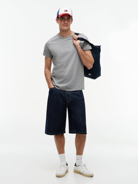 Man wearing a gray t-shirt, dark shorts, white sneakers, and a cap holding a black bag on a white background