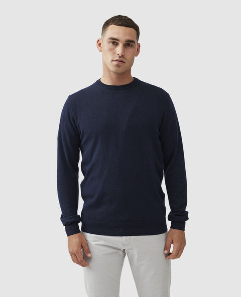 Man wearing a navy sweater and light-colored pants on a white background