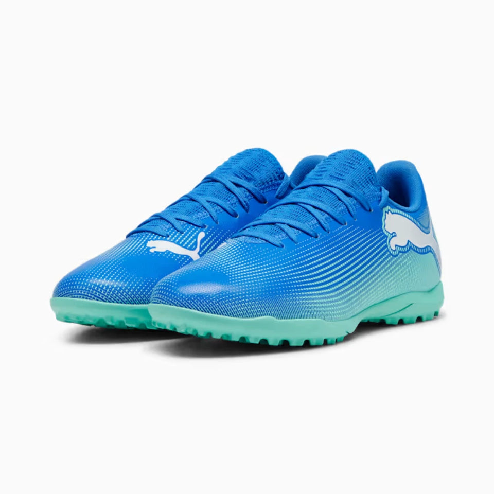 A pair of Puma turf soccer shoes in a vibrant blue gradient with a mint green sole, featuring a white Puma logo on the side.