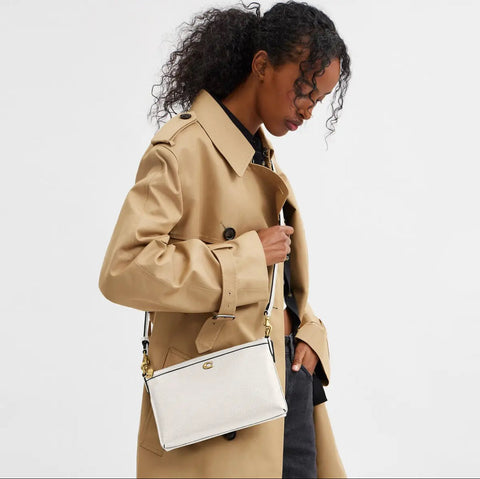 Woman wearing a beige trench coat holding a white handbag on a plain background