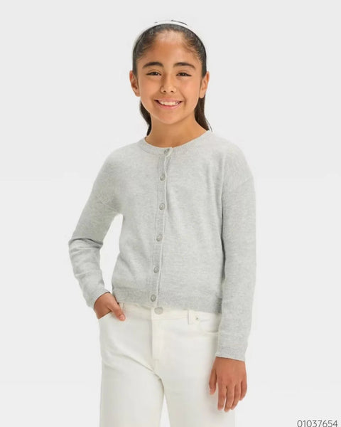 Young girl wearing a gray cardigan and white pants on a light gray background