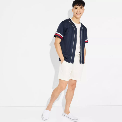 Man wearing a navy baseball jacket with red and white accents, white shorts, and white sneakers on a white background.
