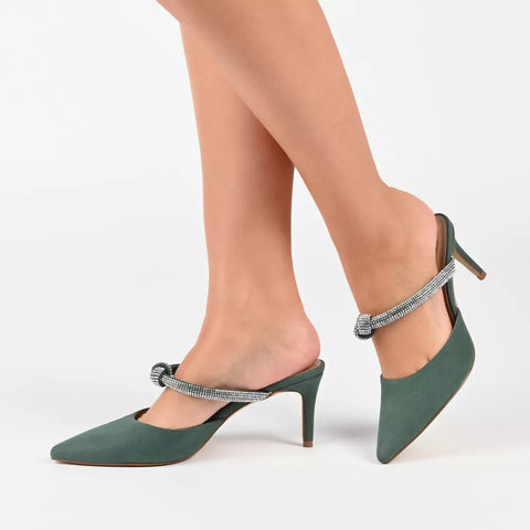 Green high-heeled shoes with embellished straps worn by a person on a white background
