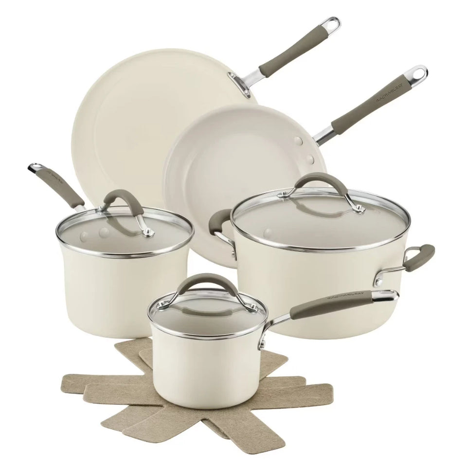 A 5-piece cream-colored nonstick cookware set with gray handles and glass lids, arranged on a white background with a beige star-shaped trivet.