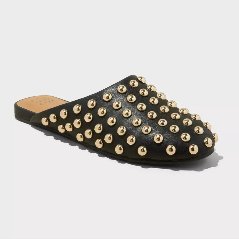 A black leather mule sandal covered in gold-tone metal studs, shown from a three-quarters angle on a light gray background.