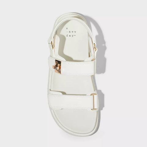 White sandal with gold buckles on a light gray background