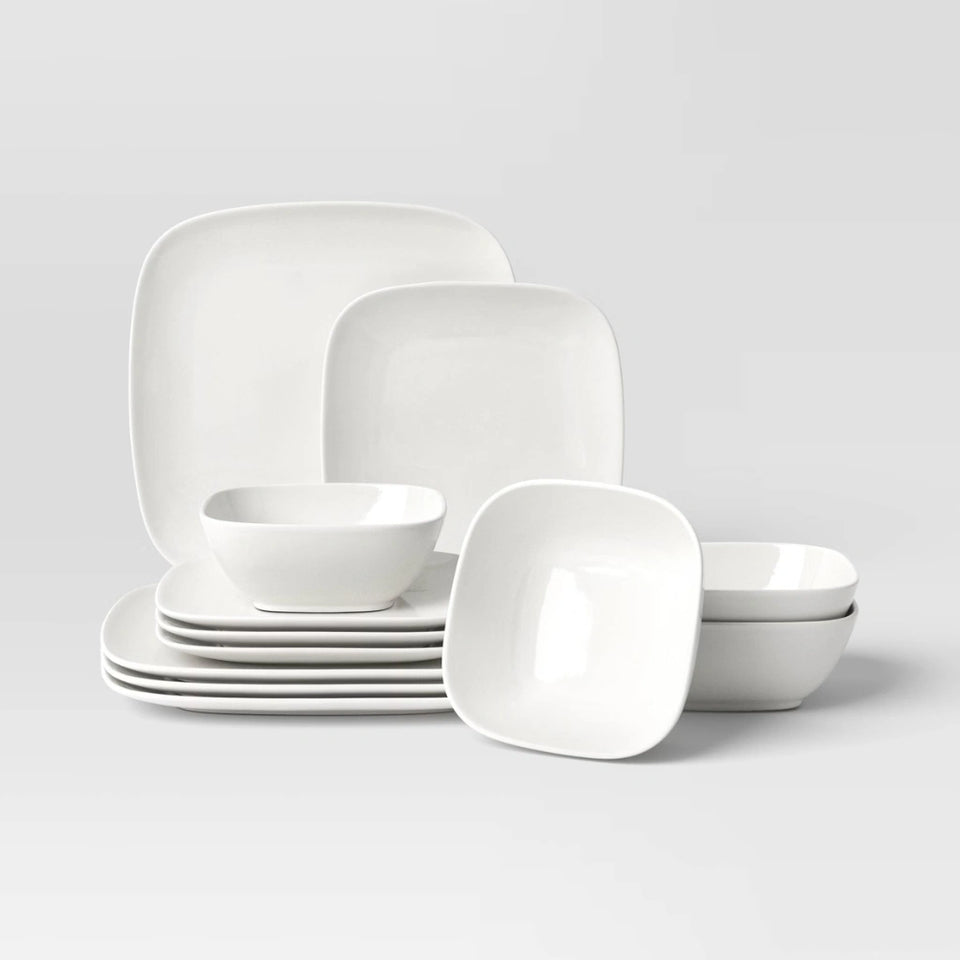 A white ceramic dinnerware set with square plates and matching bowls, arranged on a light gray studio background.