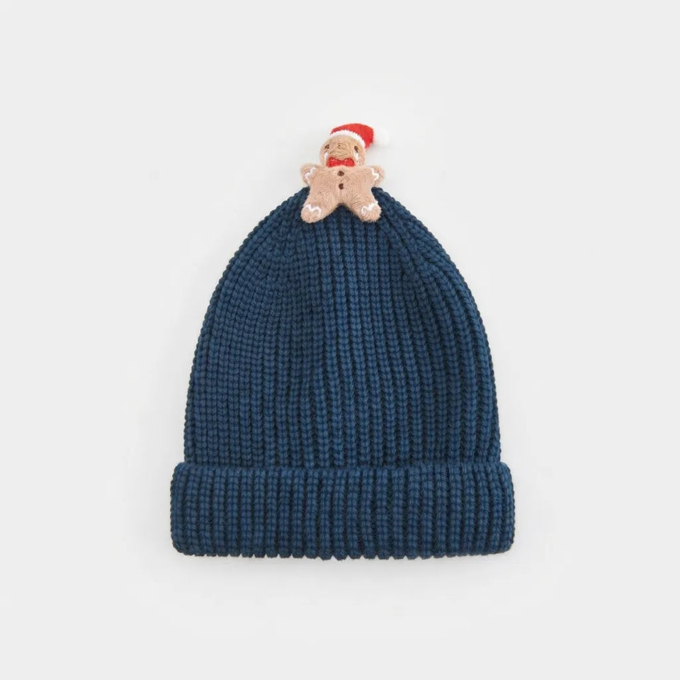 A dark blue ribbed knit beanie hat featuring a small gingerbread man ornament wearing a red Santa hat on top, set against a plain light gray background.