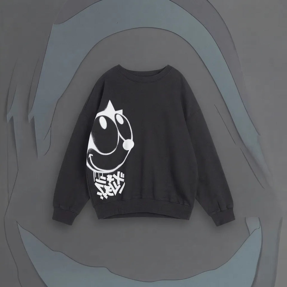 A dark gray crewneck sweatshirt featuring a white graphic of a cartoon cat head and the Japanese katakana characters 'アルイ' on the front, displayed against a stylized gray background.