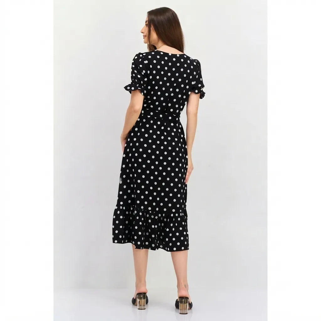 A woman wearing a black midi dress with white polka dots, shown from the back against a light gray studio background.