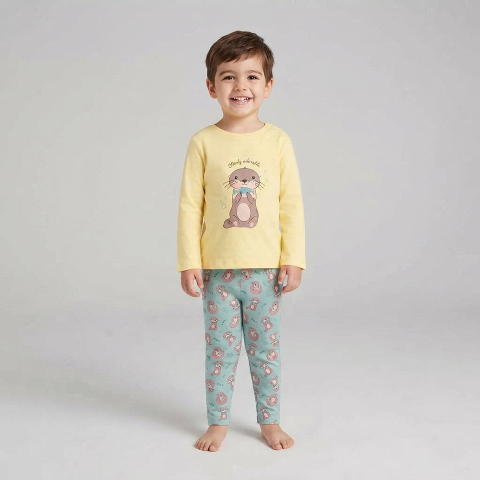 A young boy stands barefoot against a light gray studio background, wearing a pale yellow long-sleeve pajama top with a cartoon rabbit graphic and mint green patterned pajama pants.
