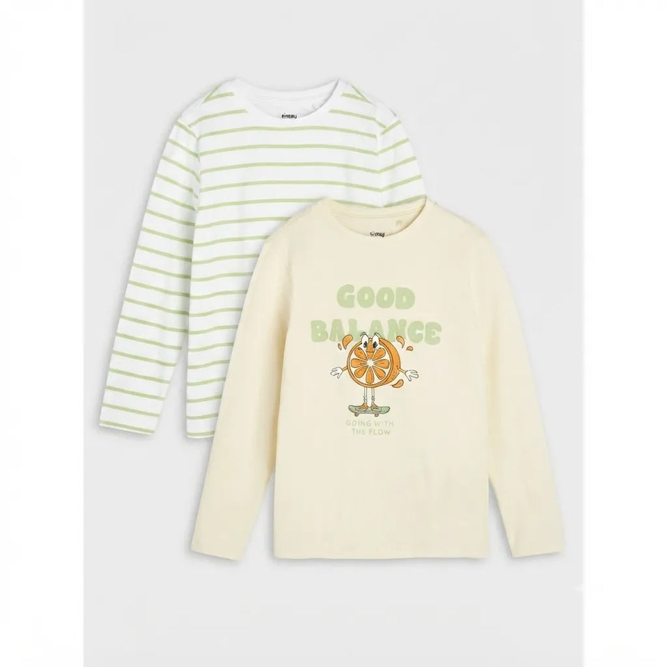 Two children's long-sleeve shirts laid flat on a light gray background. The back shirt is white with light green horizontal stripes, and the front shirt is cream with a green 'GOOD BALANCE' graphic and an orange cartoon character.