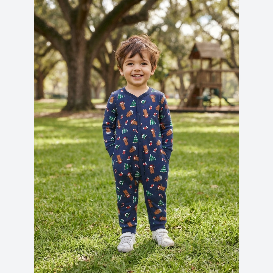 A young child standing on a grassy lawn in a park, wearing a navy blue long-sleeve jumpsuit with a colorful woodland animal print including foxes, squirrels, and pine trees, paired with white sneakers.
