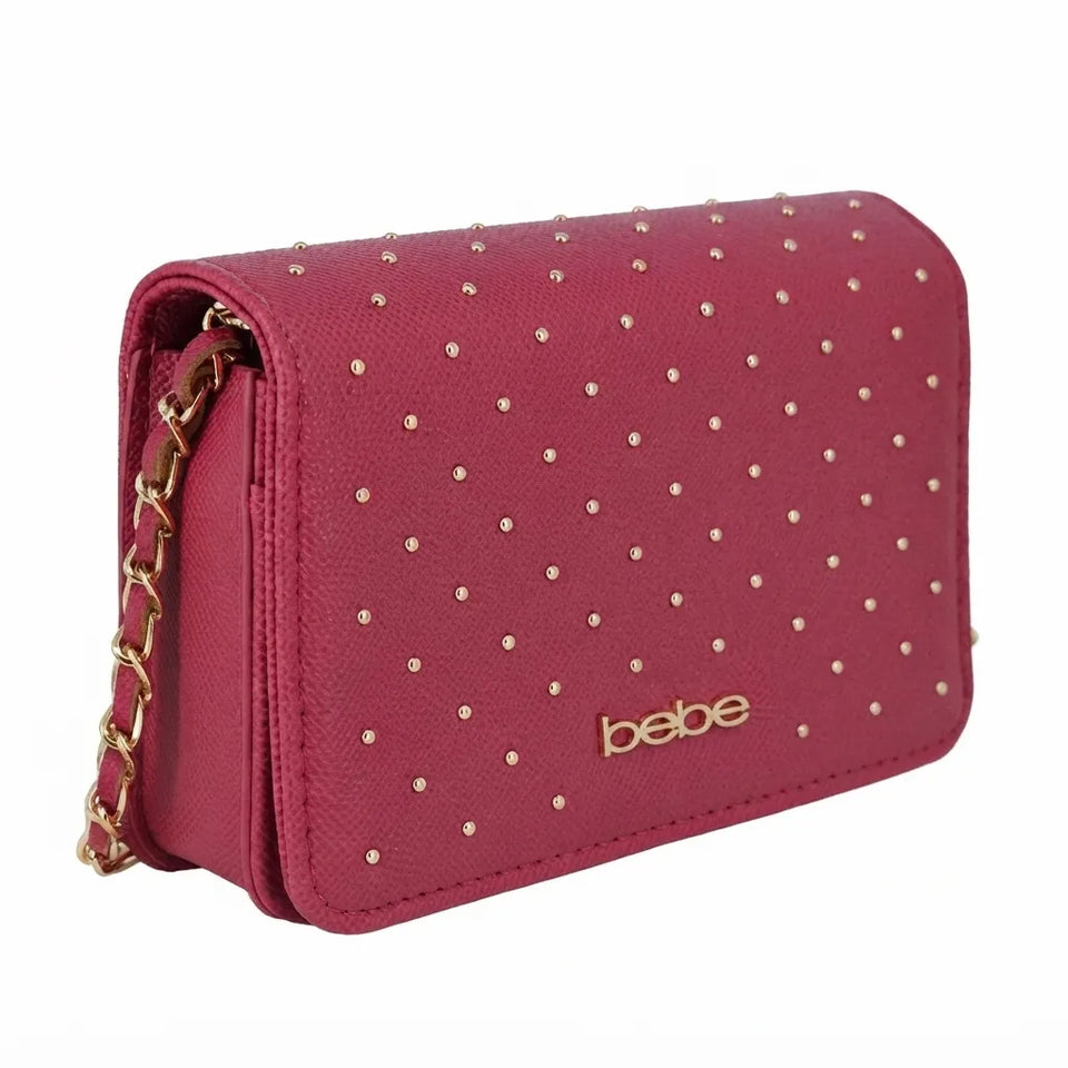 A burgundy faux-leather crossbody bag with gold studs and a gold chain strap, featuring the brand name 'bebe' in gold on the front.