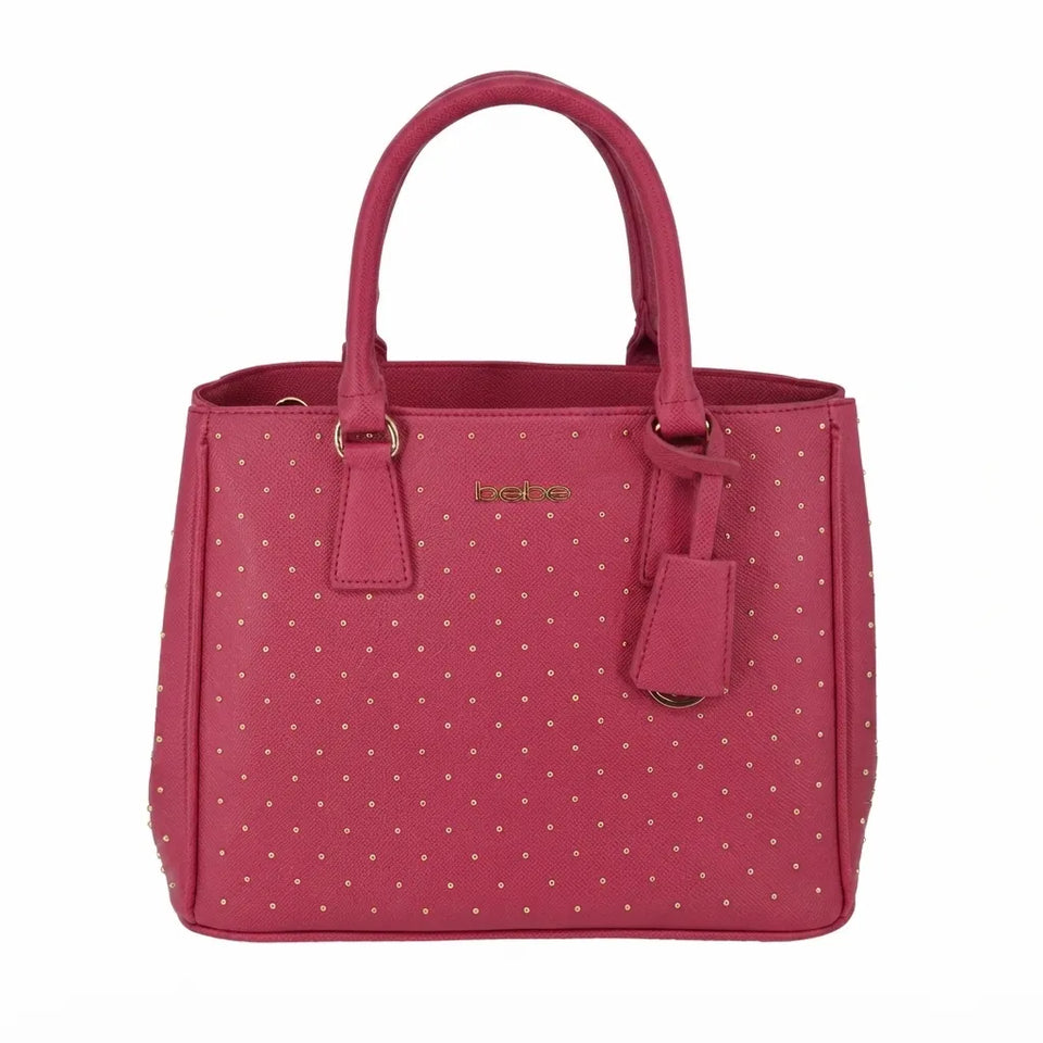 A pink faux-leather handbag with a polka-dot pattern, featuring dual top handles, a front hanging tag, and a small gold-tone logo plate on the front.