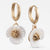 A pair of gold huggie hoop earrings with dangling white flower charms featuring textured gold centers, shown against a plain white background.