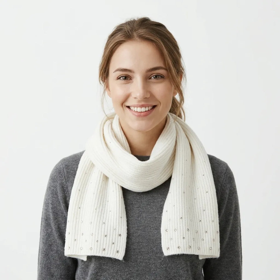 A smiling woman with light brown hair tied back wears a cream-colored ribbed knit scarf with small metallic rhinestone accents, paired with a dark gray sweater against a plain white background.