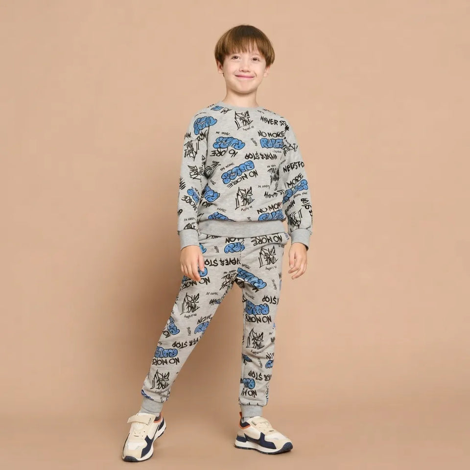 A young boy modeling a light gray two-piece tracksuit with a blue and black graphic print, standing against a solid beige background.