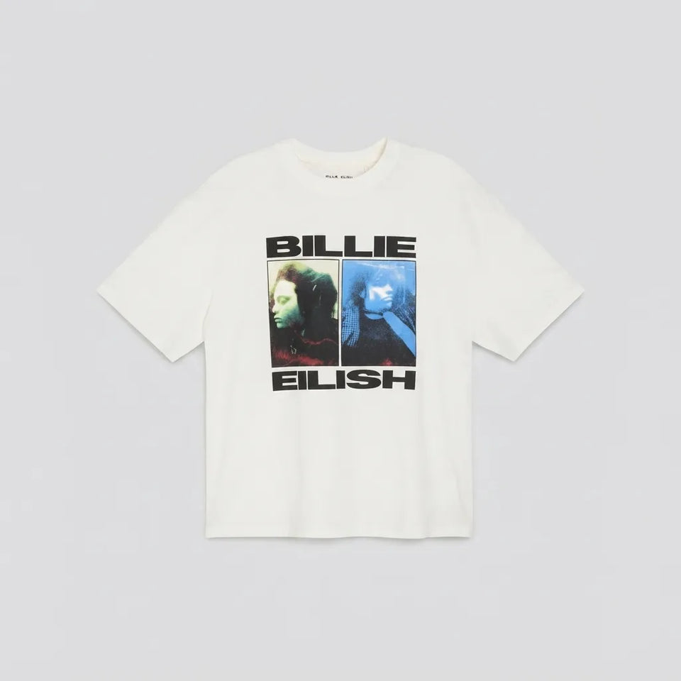 An off-white short-sleeve t-shirt featuring a graphic print of Billie Eilish with the text 'BILLIE EILISH' and two portrait panels, displayed flat against a light gray background.