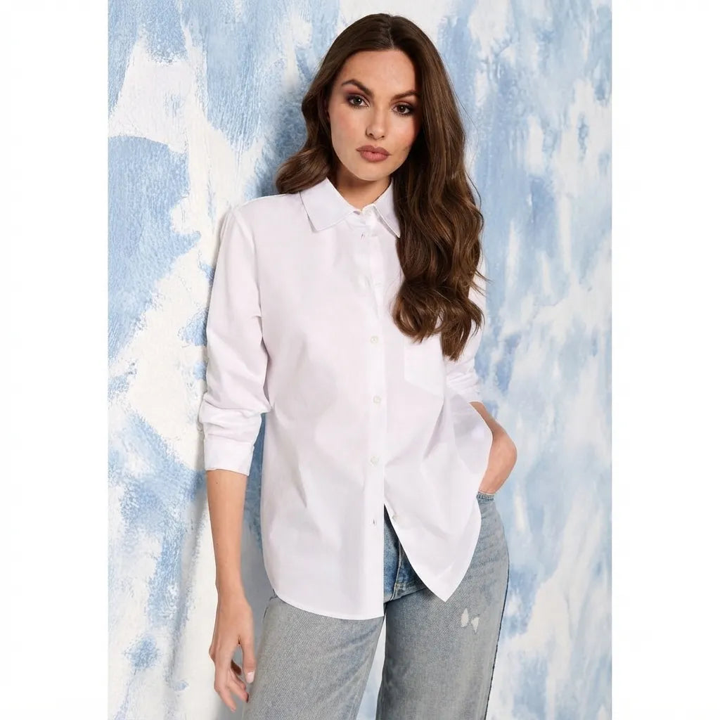 A woman wearing a white long-sleeve button-up shirt and light gray jeans, standing against a textured blue and white background.