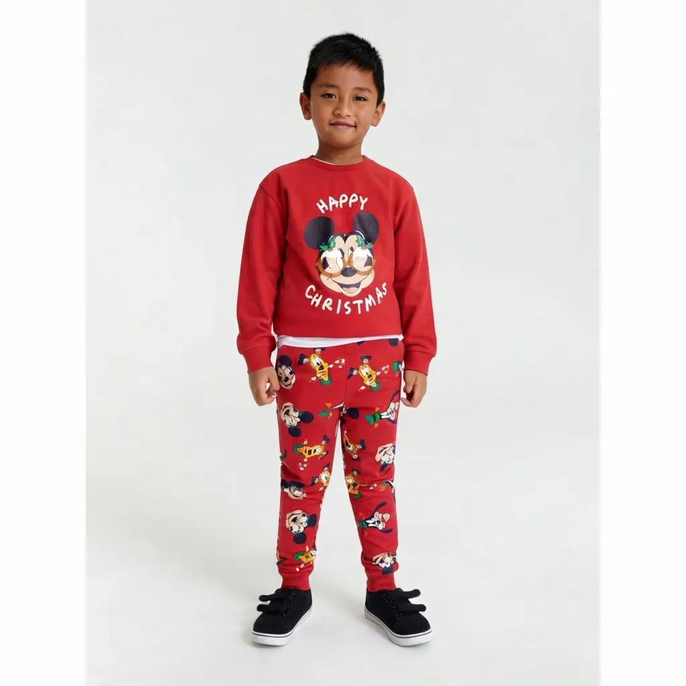 A young boy modeling a red Christmas-themed pajama set featuring a 'Happy Christmas' sweatshirt with a Mickey Mouse graphic and matching patterned pants, set against a plain light gray background.