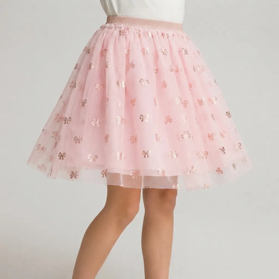 A pink tulle tutu skirt with metallic rose gold bow patterns, shown on a model from the waist down against a light gray background.