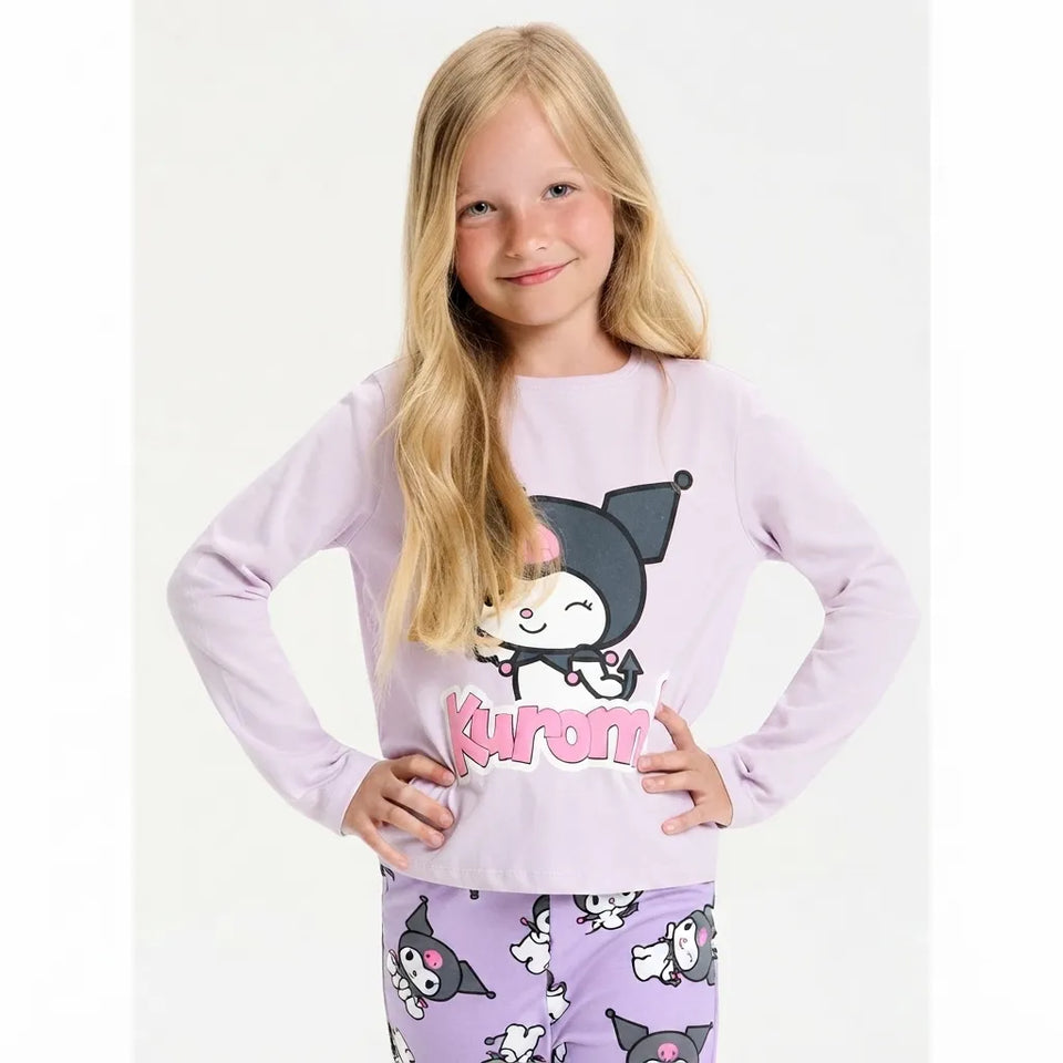 A young girl with long blonde hair wearing a light purple long-sleeve pajama top with a Kuromi graphic and matching patterned pajama pants, posing against a white studio background.