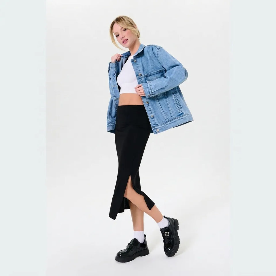 A woman modeling a light blue denim jacket over a white crop top, paired with a black midi skirt, white socks, and black leather loafers, against a plain white studio background.