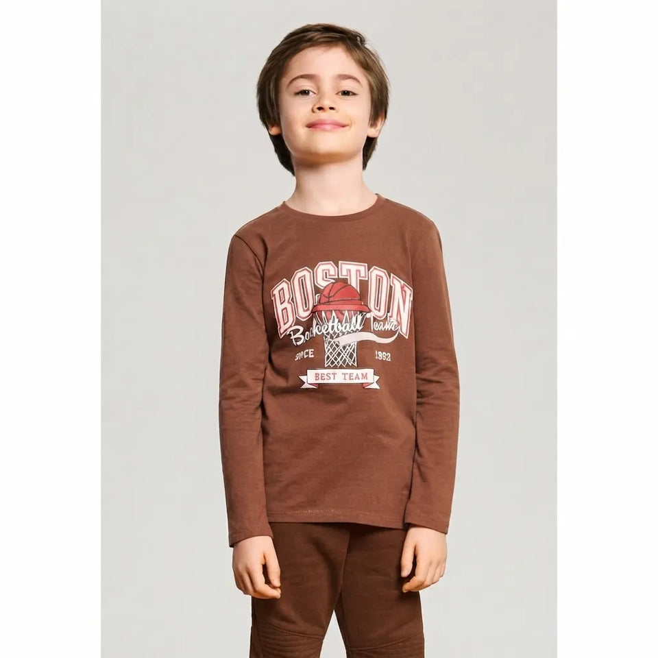 A young boy wearing a brown long-sleeve crewneck sweatshirt with a 'BOSTON BASKETBALL' graphic on the front, paired with matching brown sweatpants, set against a plain light gray studio background.