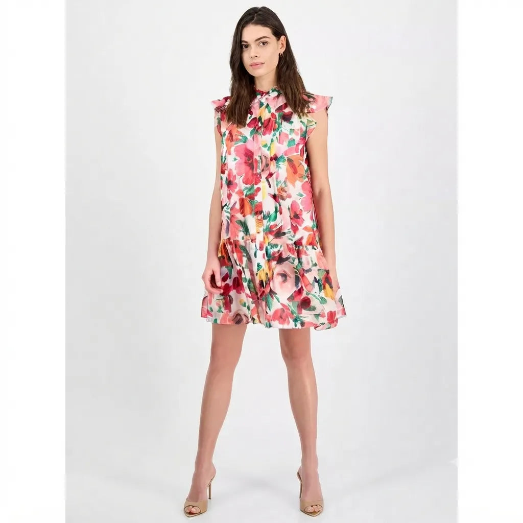 A woman modeling a sleeveless tiered mini dress with a vibrant multicolor floral print, set against a plain light gray studio background.