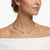 A close-up of a woman's neck and upper chest wearing a delicate silver-toned open choker necklace with two small heart-shaped crystal pendants, against a clean white background.