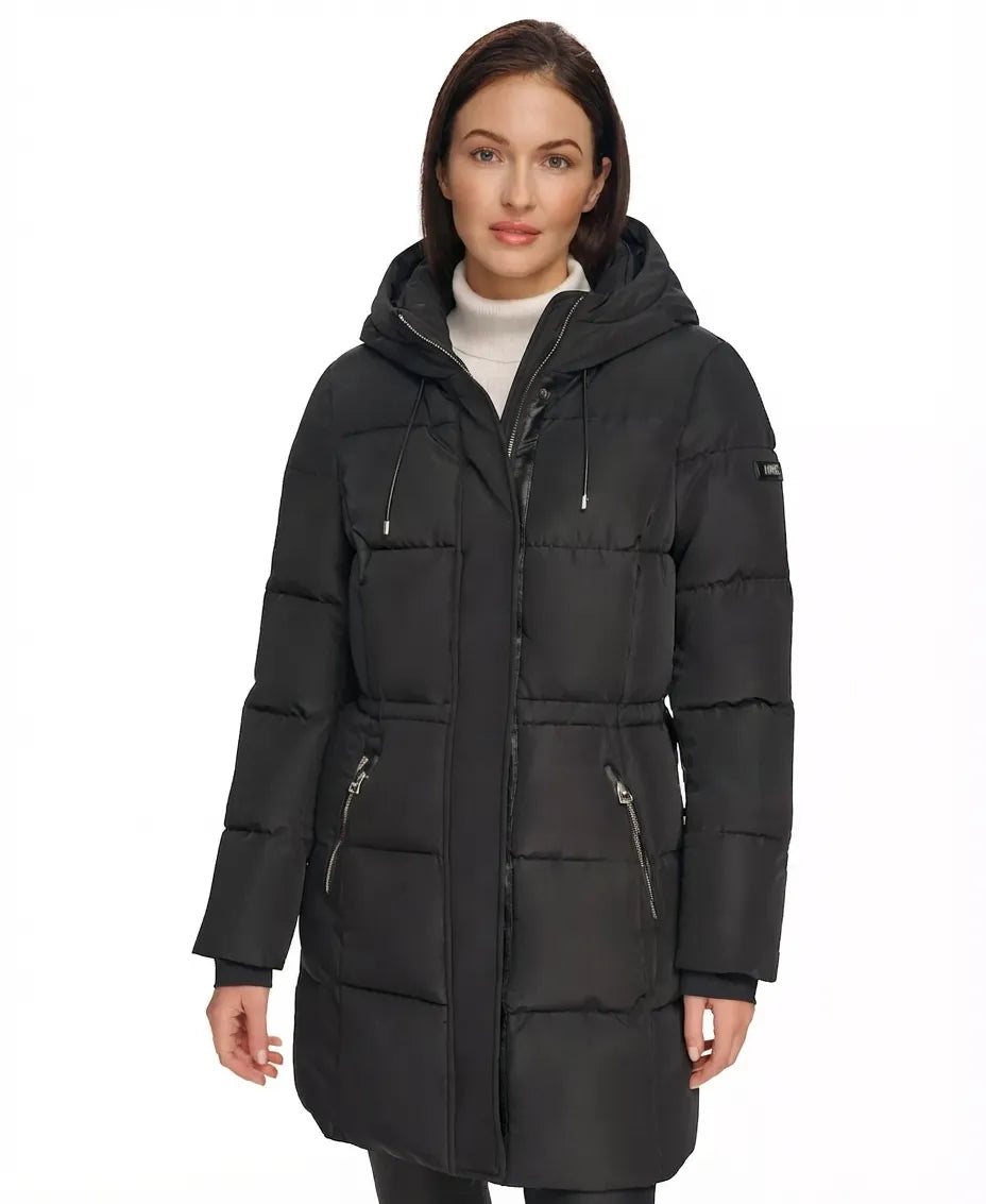 A woman wearing a black hooded puffer coat with horizontal quilting, front zipper, and zippered hand pockets, photographed against a plain white studio background.